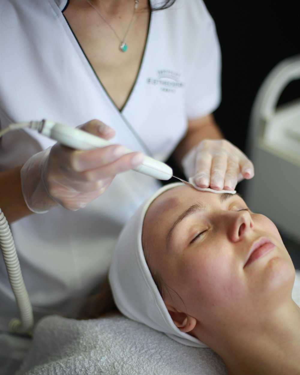 A clinician performing a facial treatment on a patient in a clinic room.